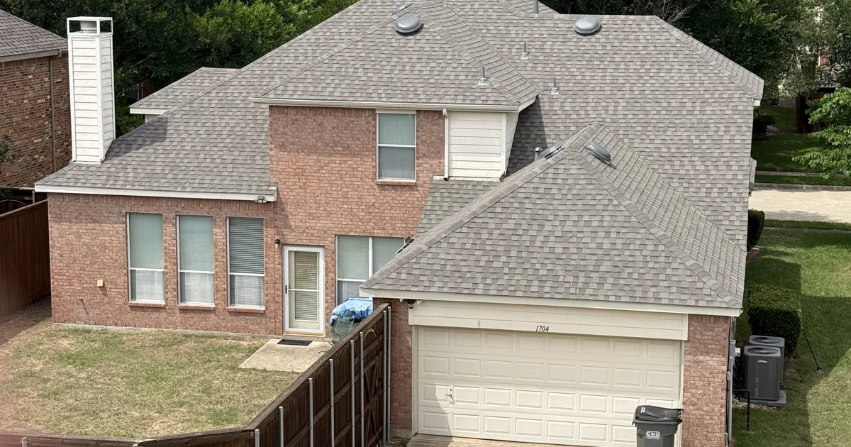 Aerial drone photograph of a North Texas custom home reroof in progress by Frame Restoration, with synthetic underlayment fully installed and architectural shingle bundles staged across the roof planes under a clear DFW sky