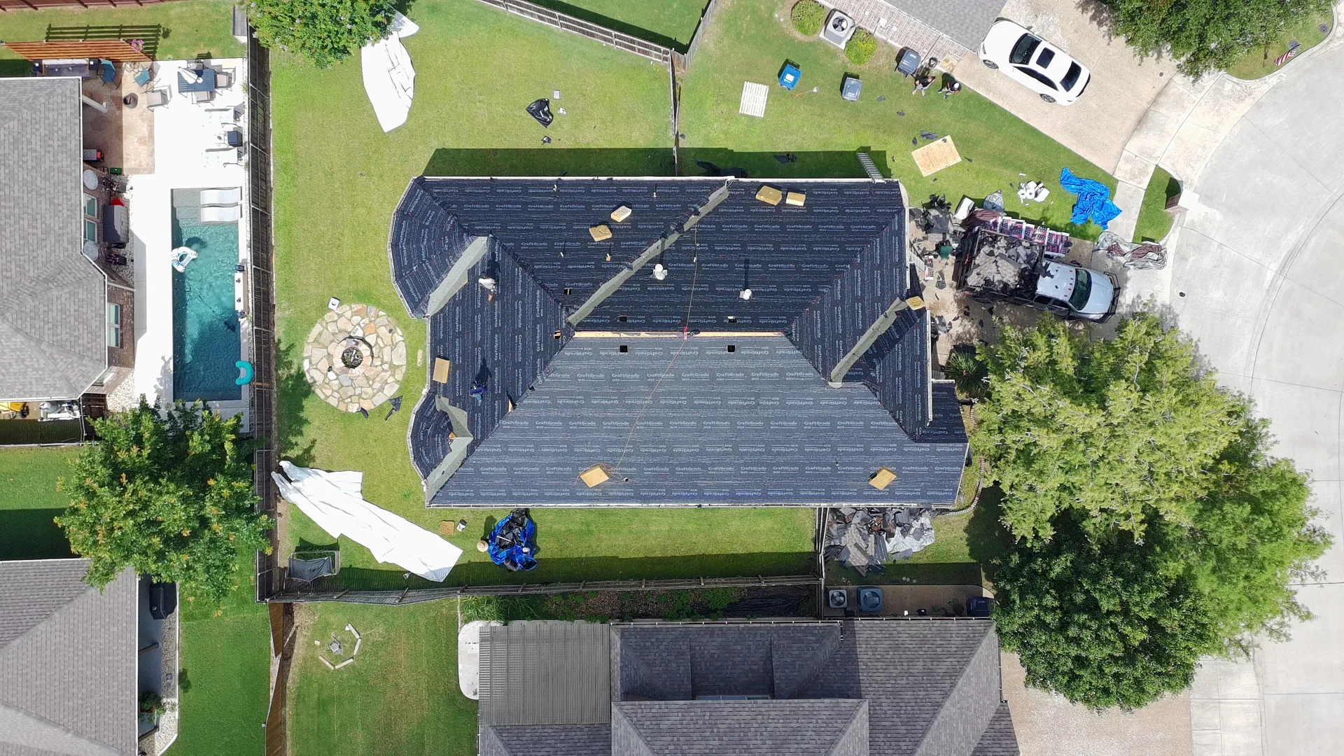 Aerial drone view of an in-progress Frame Restoration roof replacement in McKinney, Texas, with synthetic underlayment installed across the roof planes and a crew working
