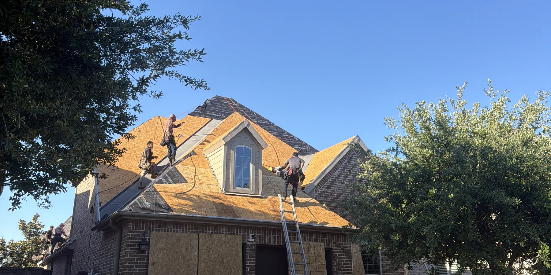 Frame Restoration crew working on a residential roof replacement in The Colony, Texas, with exposed plywood decking visible after the old shingles have been torn off